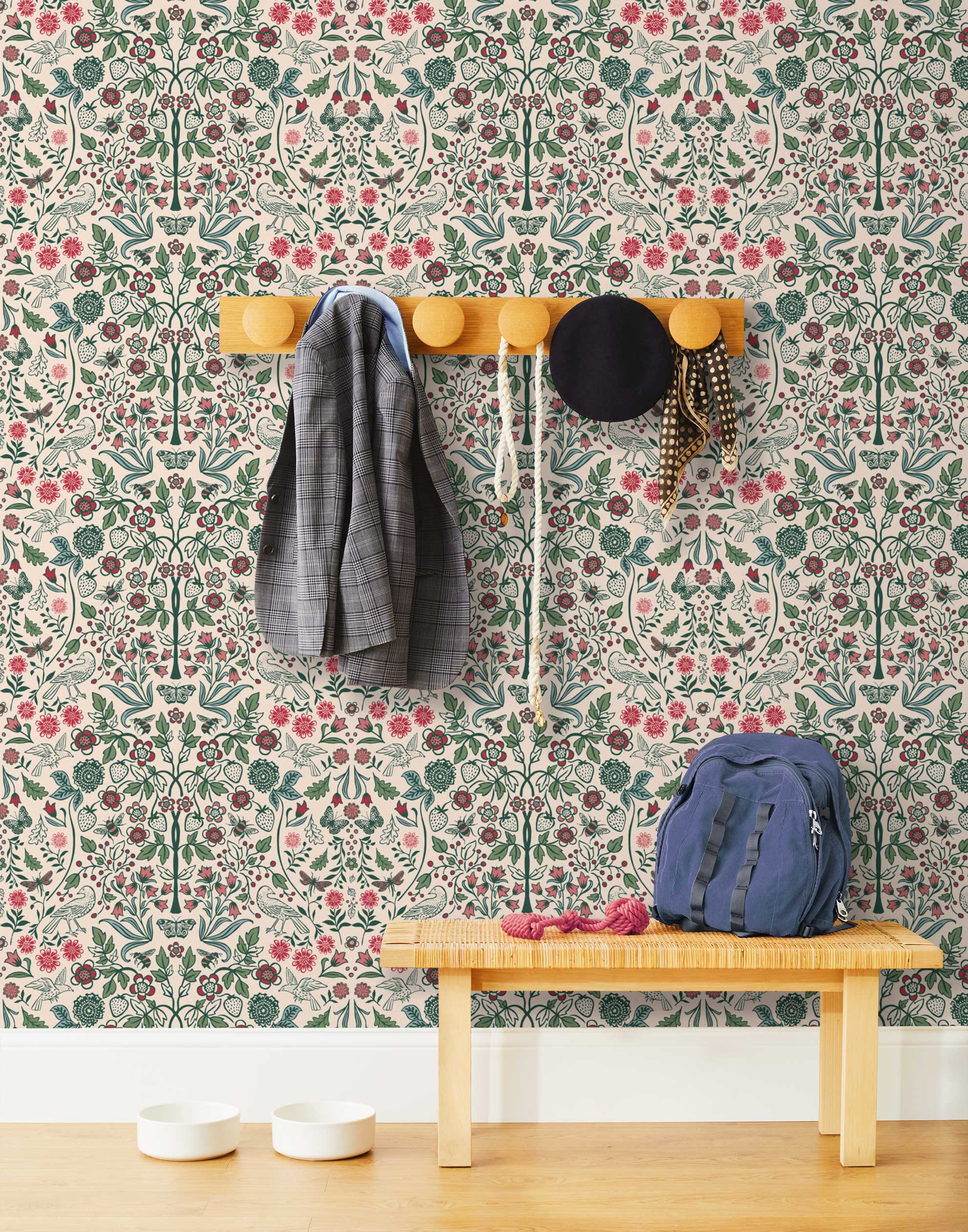 Nora (Blush) wallpaper features a garden of bees, birds, strawberries, and flowers in green, blue and red on a pink background.