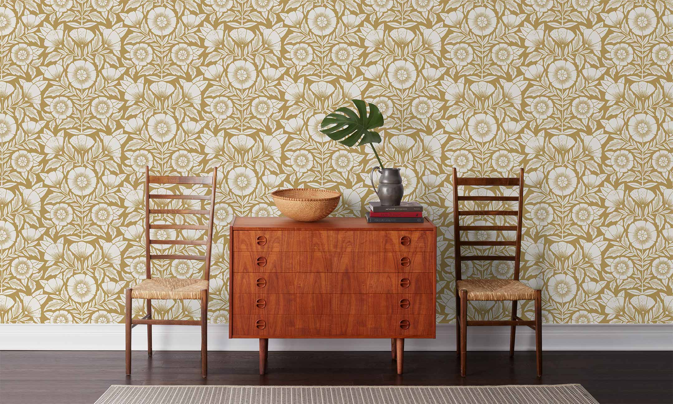 Conservatory wallpaper featuring stylized petals and leaves dervived from a block-print technique was designed by Katharine Watson for Hygge & West. Featuring white flowers on an ochre yellow wallpaper background.